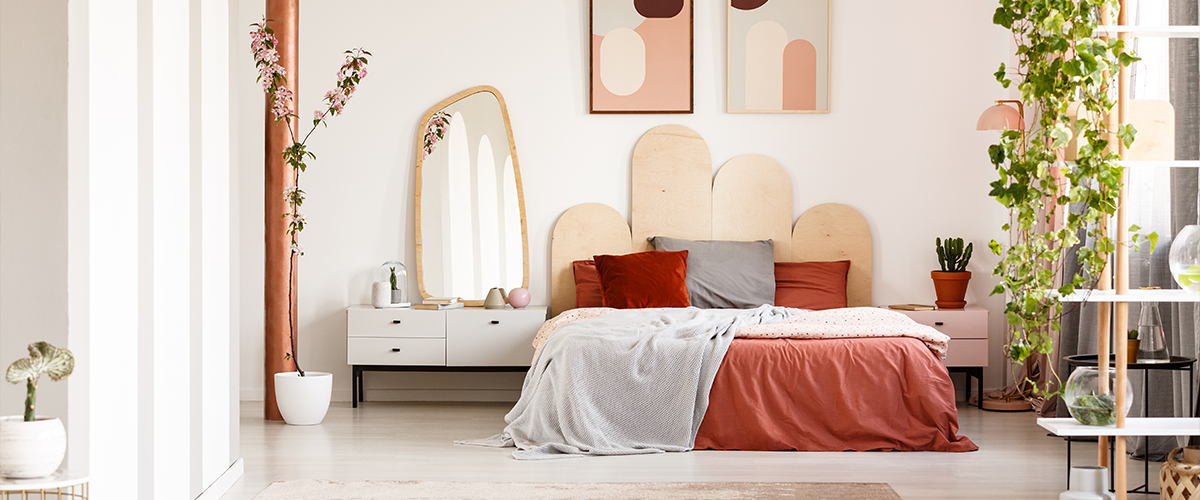 A modern bedroom featuring a unique wooden headboard, abstract art, and a mix of warm hues.