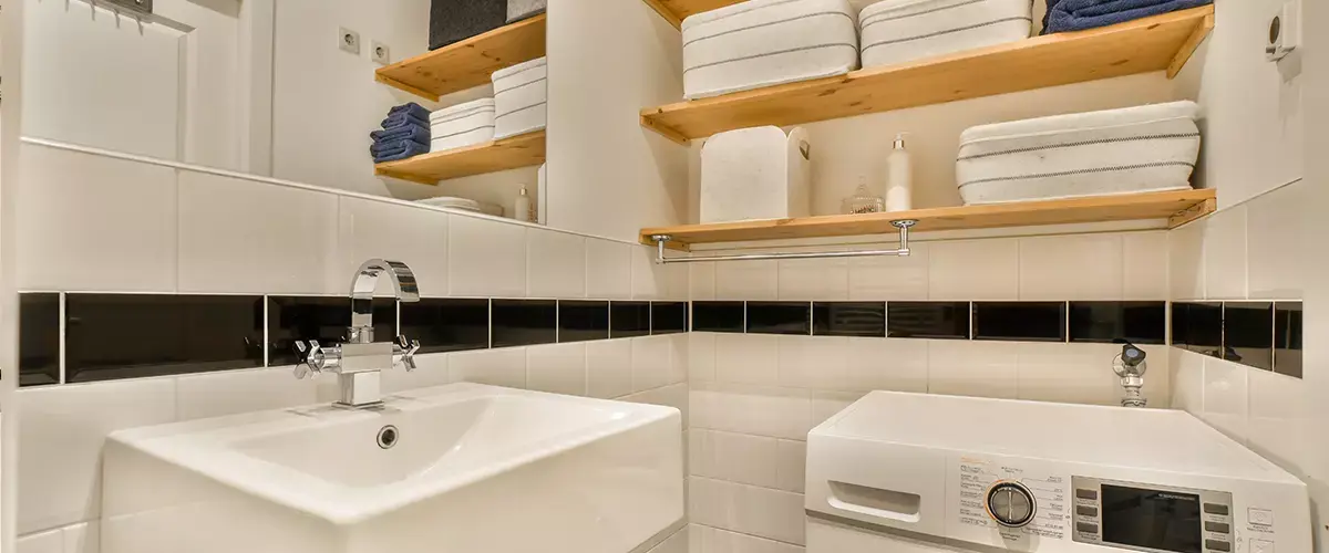 a washer and dryer in a small bathroom with black tiles on the floor, white walls and wooden shelvings