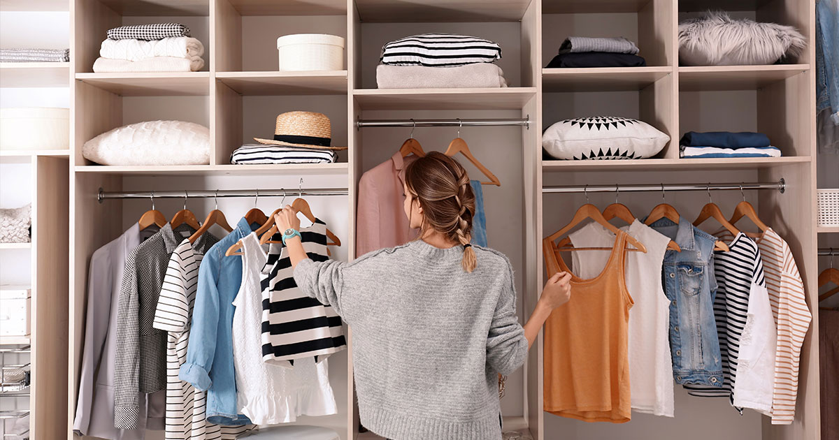 Woman organizing clothes in a neatly arranged closet system with shelves and hangers, showcasing a modern closet design