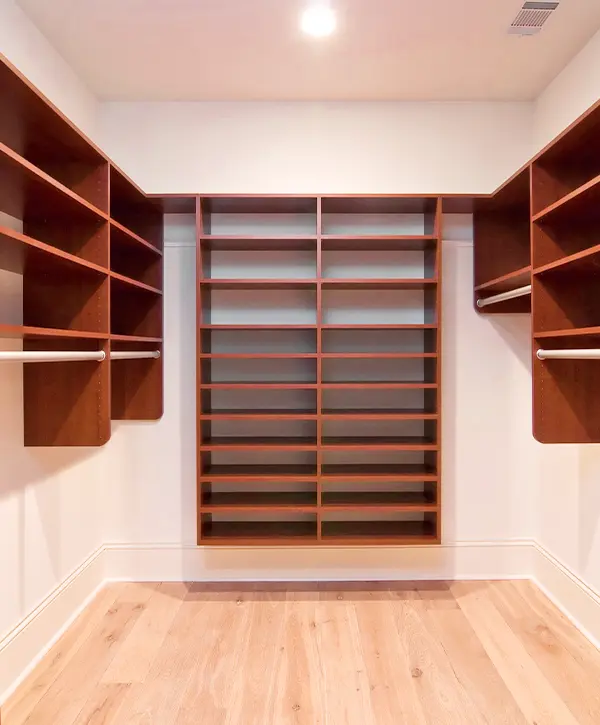 Spacious walk-in closet with empty wooden shelving, hanging rods, and light hardwood flooring