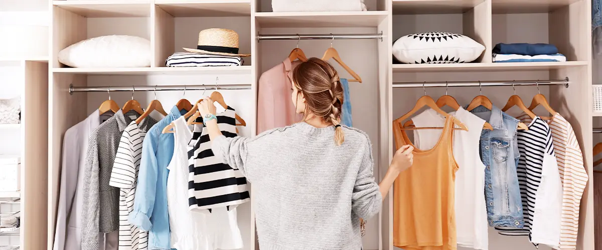 Woman sorting clothes on hangers in a neatly organized modern walk-in closet with shelves and storage boxes