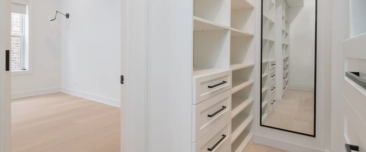 Modern walk-in closet with open shelving, a large mirror, and white cabinetry for elegant home organization solutions.