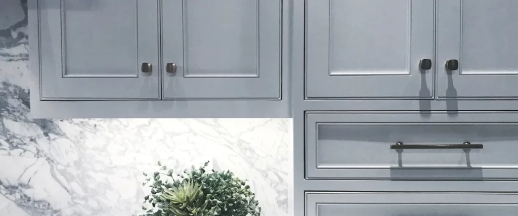 A modern kitchen featuring blue shaker-style cabinets with bronze hardware, set against a white marble backsplash with subtle gray veining