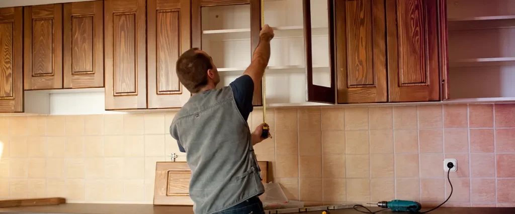 Kitchen cabinet installation in progress, carpenter measuring wooden upper cabinets for a home renovation project.